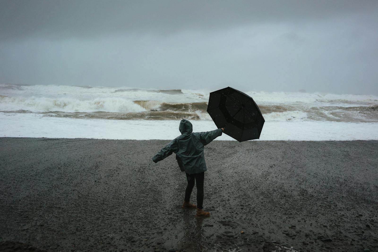 Person braving a storm on the beach holding an umbrella against powerful waves.